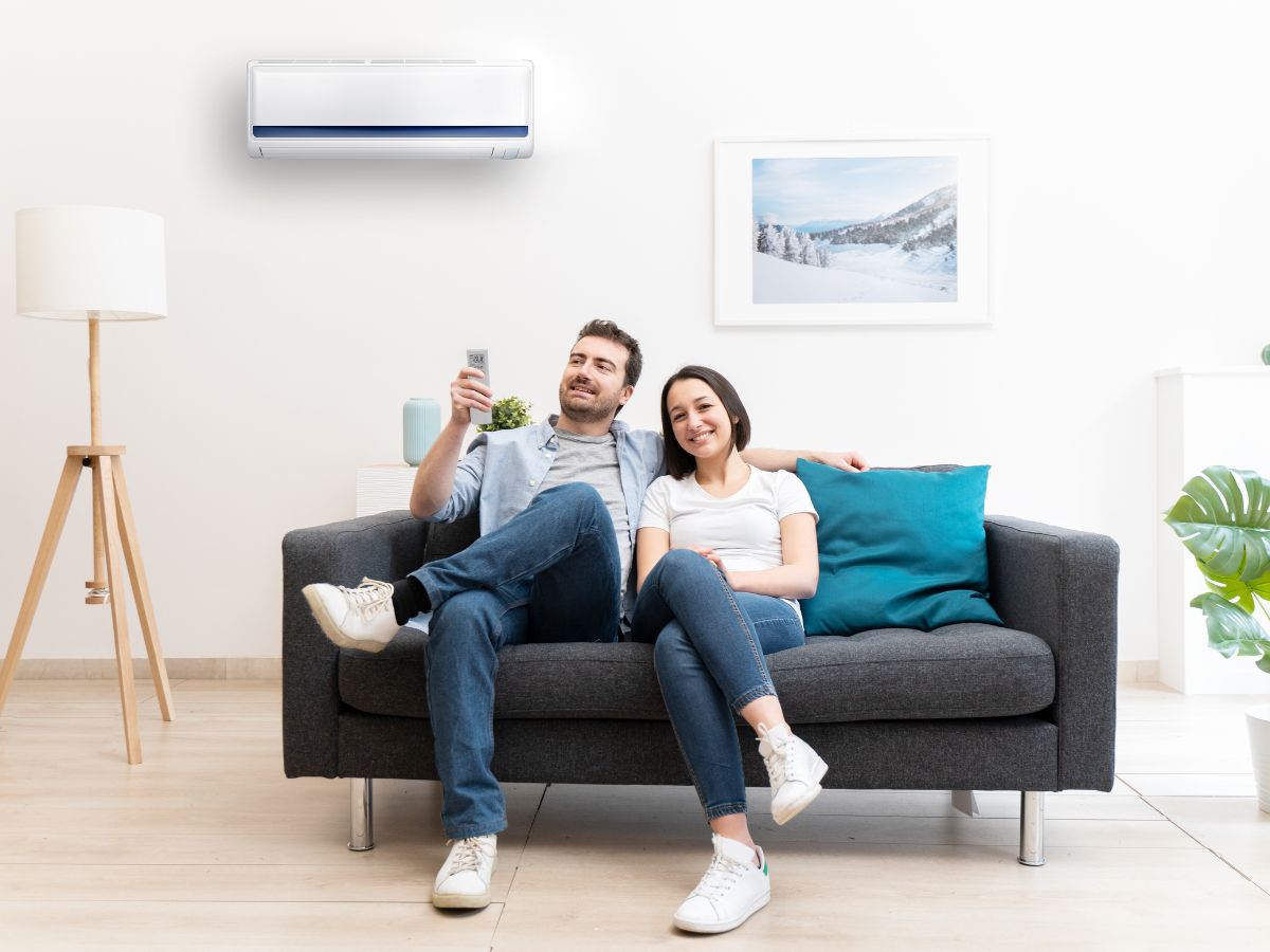 a man and a woman sitting on a couch in a living room with the air conditioning on