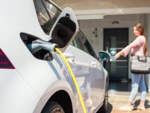 close up shot of an EV charger in an EV vehicle. Woman standing in the background using her keys to lock the car.